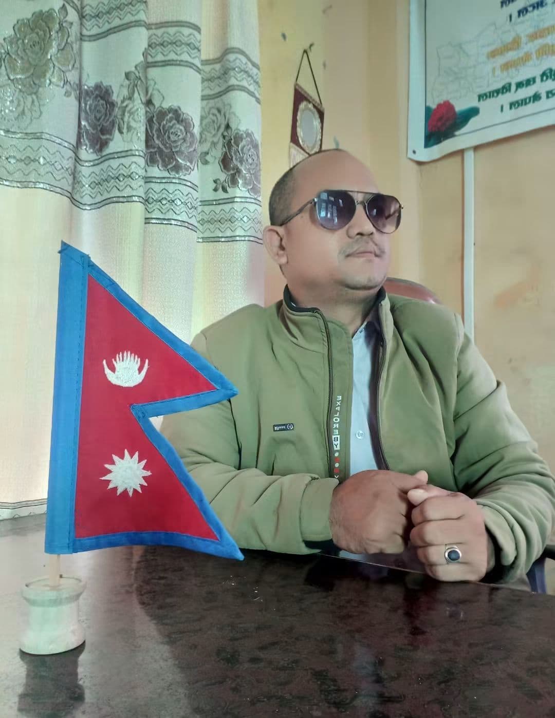 Tej Prakash GC seated at a desk beside a Nepali flag
